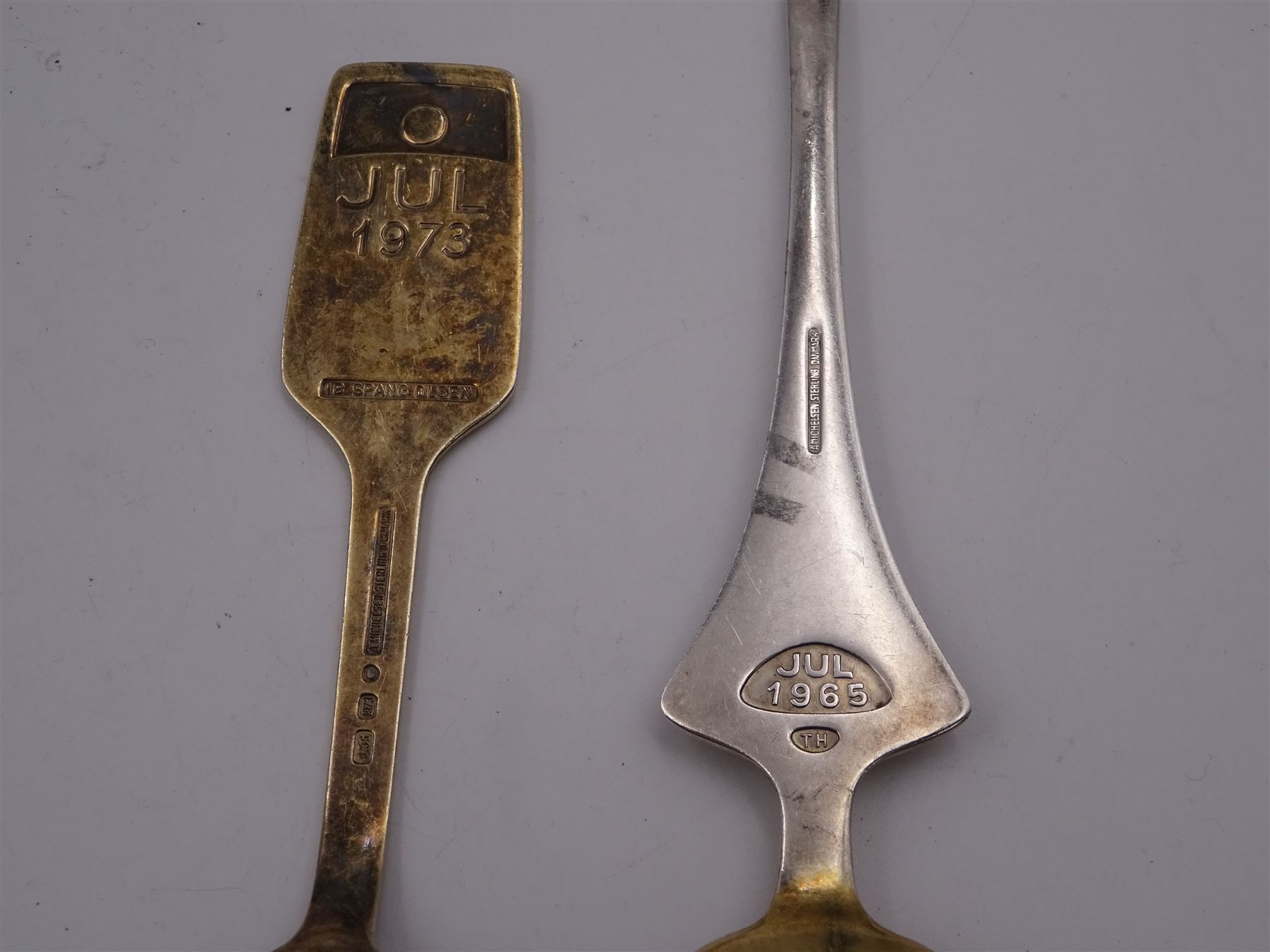 Two Danish silver-gilt year spoons by Georg Jensen, the first example decorated with enamel blue cornflower motif, dated 1972, in original pouch, the second example decorated with enamel pink briar rose motif, dated 1976, in original box, each impressed on underside RA AB, Sterling Denmark, and marked for Georg Jensen, together with two further examples by A.Michelson, the first with orange enamel fan design, dated 1965, impressed on underside A.Michelsen Sterling Danmark, TH, the second with enamel family scene, dated 1973, impressed on underside 925 S A.Michelsen Sterling Danmark, B Spang Olsen, approximate gross weight 6.11ozt (190.4 grams)