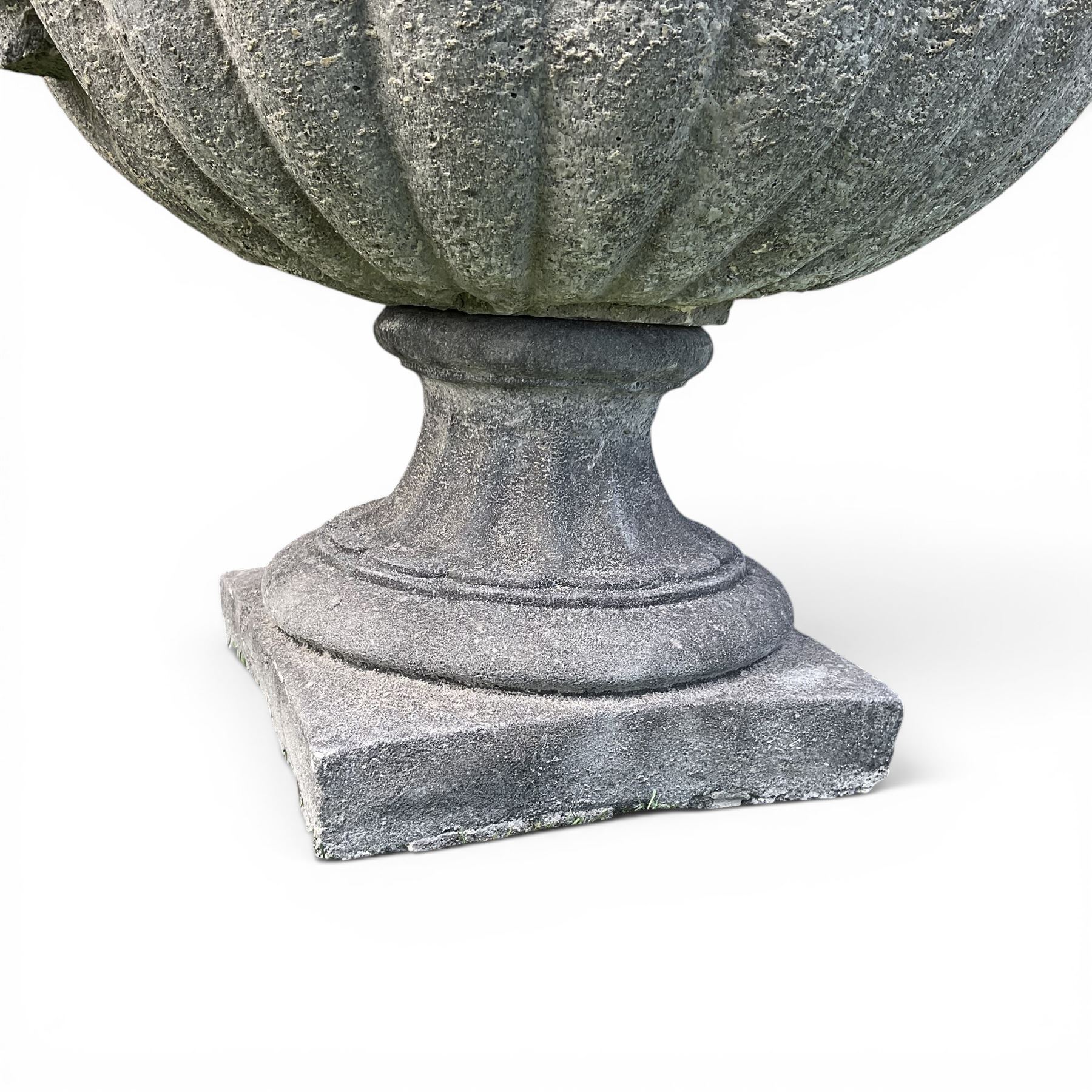Pair of squat cast stone garden urns of kylix form, gadrooned body with twin pierced scrolling handles, fluted socle on square base