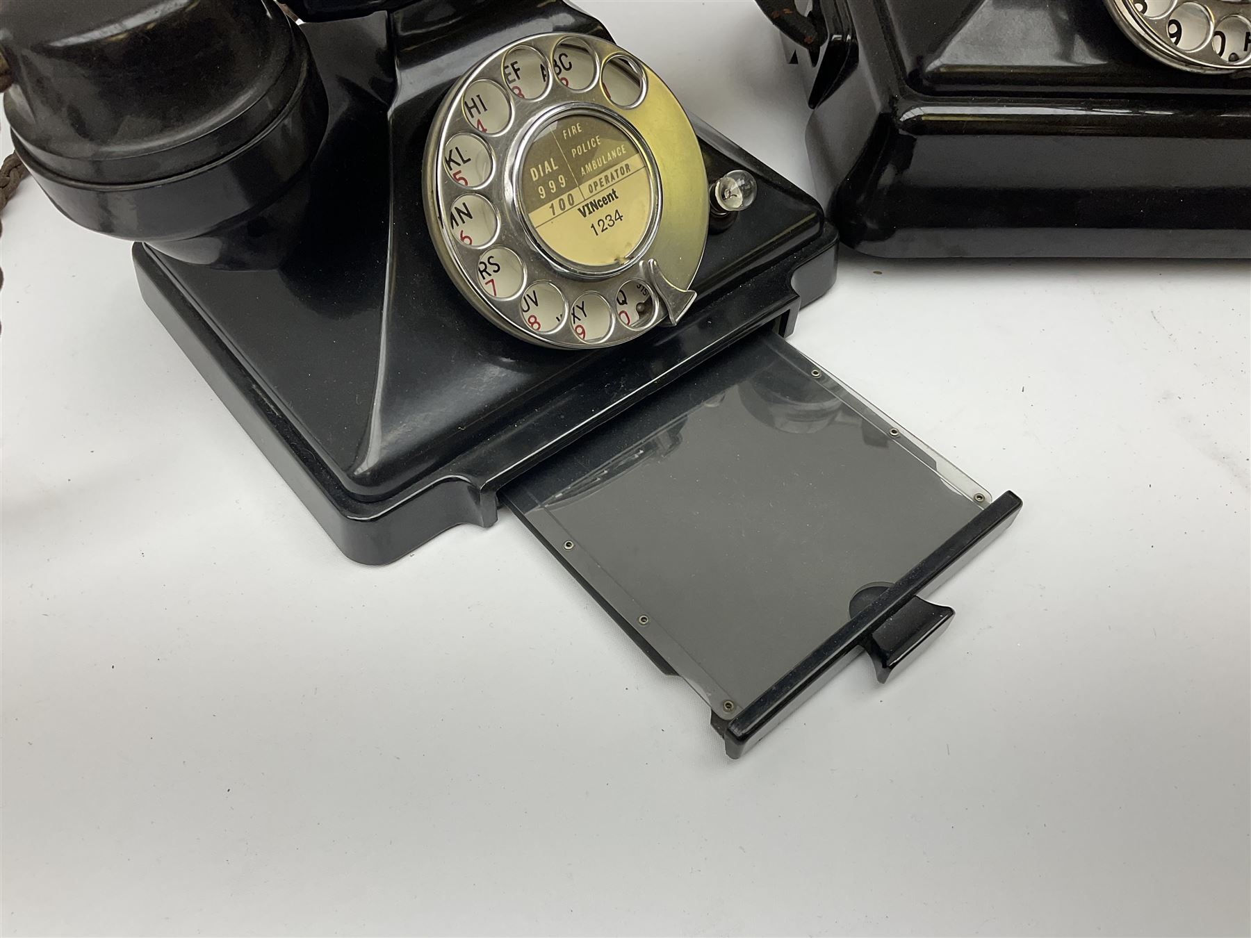 Two black Bakelite telephones of pyramid form with rotary dials, comprising The Telephone Demonstration Set model. 6al with base drawer and light bulb, and another larger with G.P.O FWR 58/2 stamped marks beneath, largest H18cm W20cm D16cm