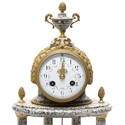 French- early 20th century portico clock garniture, 8-day drum movement decorated with laurel leaves to the glazed bezel and surmounted by a decorative urn with scroll handles, raised by four matching columns on a granite effect oval base with toupee feet, convex enamel dial with gilt pierced hands, Arabic numerals, minute markers and a garland of flowers, twin train Parisian rack striking movement, striking the hours and half hours on a bell. With a sunburst pendulum and key and a matching pair of two-light candelabra.