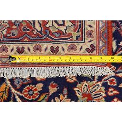 Central Persian Kashan hand-knotted rug, indigo field with central lobed medallion with pendants issuing scrolling arabesque of palmettes, flowering vines, and foliate tendrils, with conforming spandrels, with vine border and framed by guard stripes in tones indigo, ivory and madder red, with cotton fringe ends 