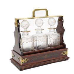 Amboyna three bottle tantalus, the cut glass spirit decanters decorated with raised natura...
