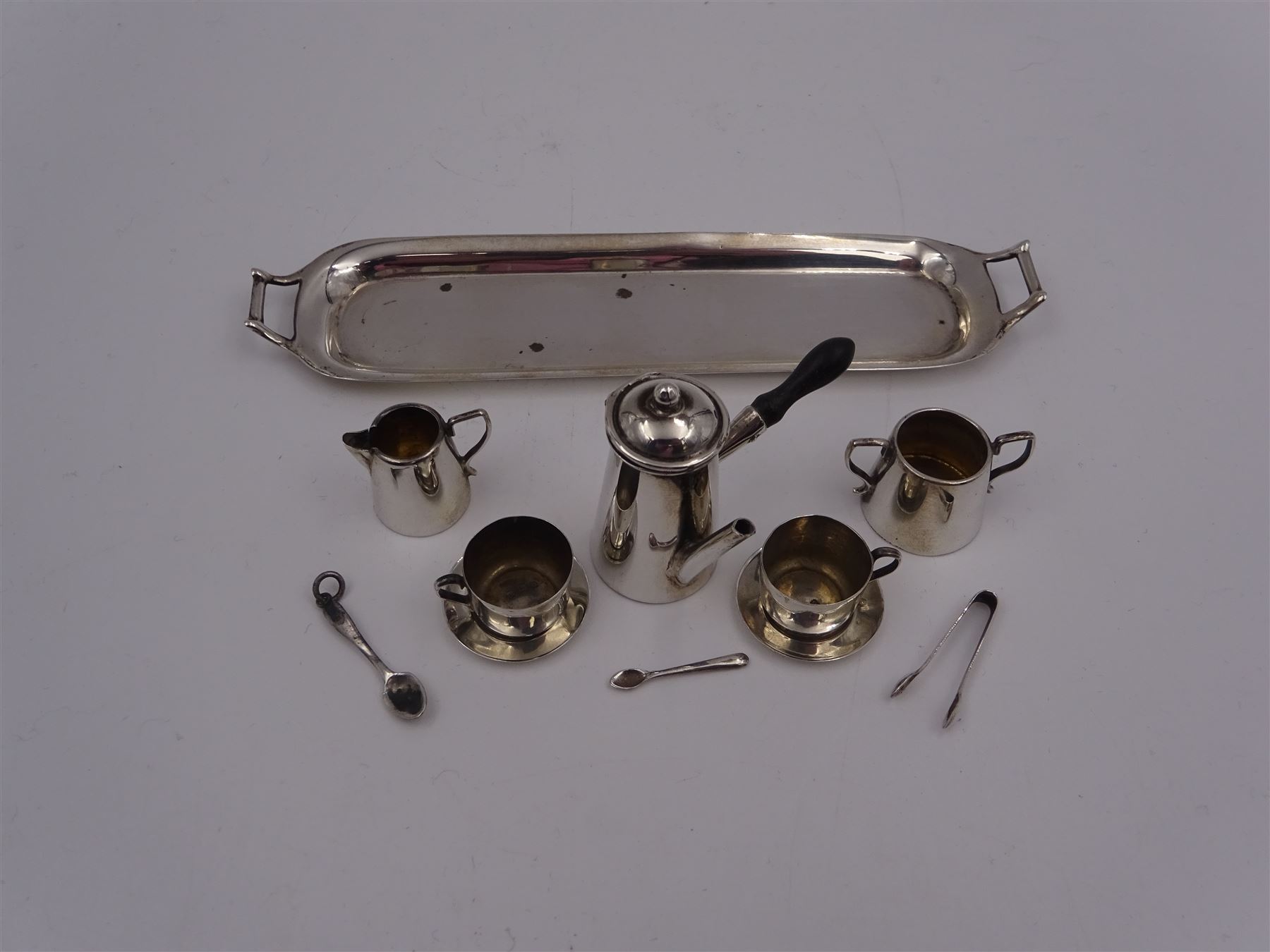 Edwardian miniature silver tea set, comprising hot chocolate pot, two cups and saucers, milk jug, sugar bowl and tray, hallmarked Cornelius Desormeaux Saunders & James Francis Hollings (Frank) Shepherd, Chester & Birmingham 1908, with two spoons and pair sugar tongs, hot water pot H3.8cm