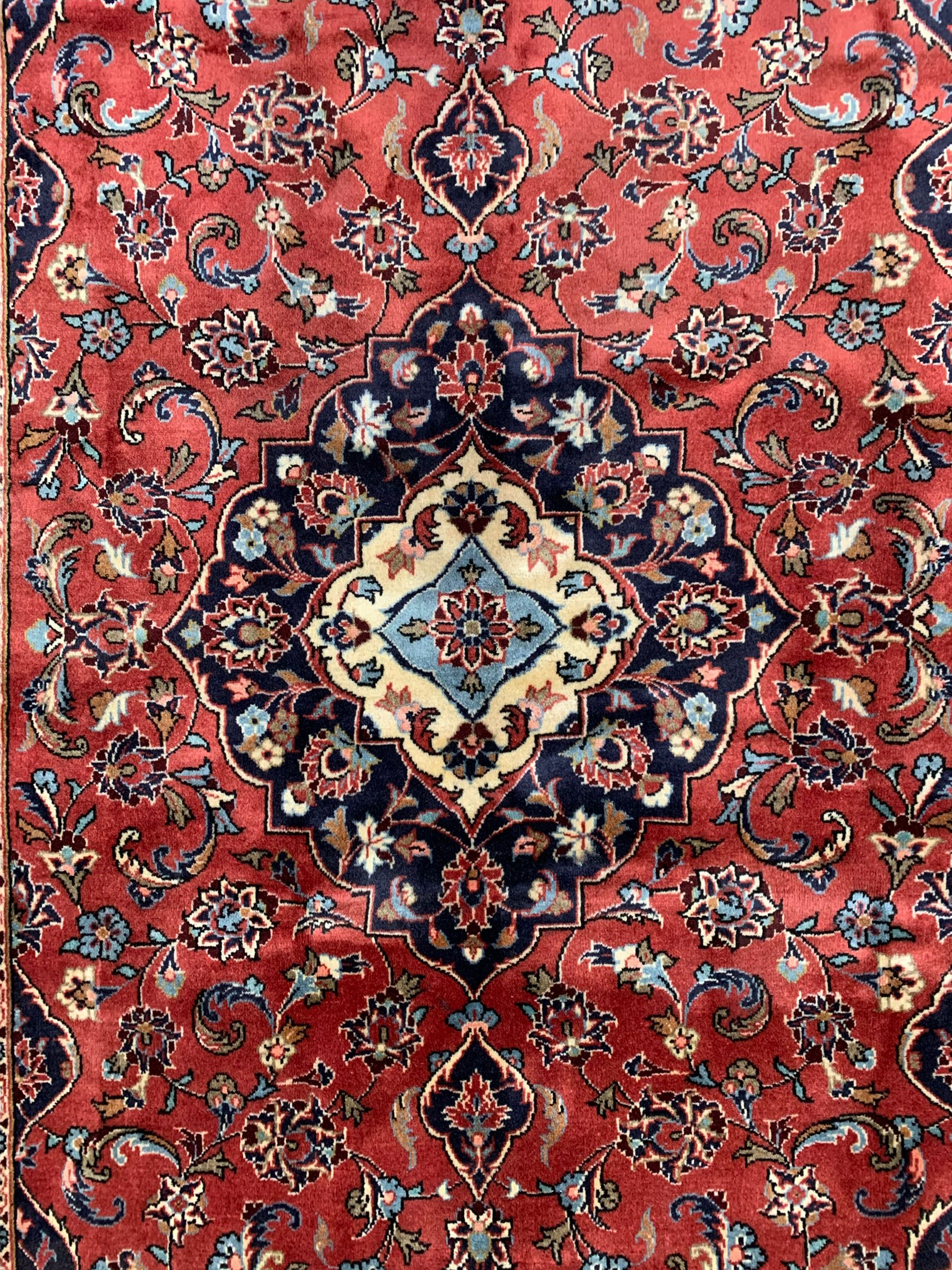 Persian Ardakan crimson ground rug, the field with shaped floral design medallion surrounded by curled leafy branches, scrolling border with stylised plant motifs