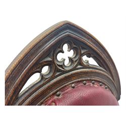 Late Victorian Gothic-revival armchair, arched crest rail carved with tracery and trefoil detail, padded circular back and seat, brass studded burgundy leather upholstery, shaped armrests with scrolled terminals, on square tapering supports