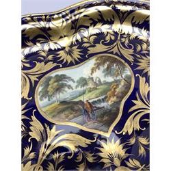 Pair of early 19th century Derby dessert dishes, 1806-1825, of kidney form, each hand painted with pastoral views within a gilt foliate border upon a dark blue ground, each inscribed verso 'Near Egginton Derbyshire', and 'In Italy', with painted marks beneath, L25.5cm H20cm