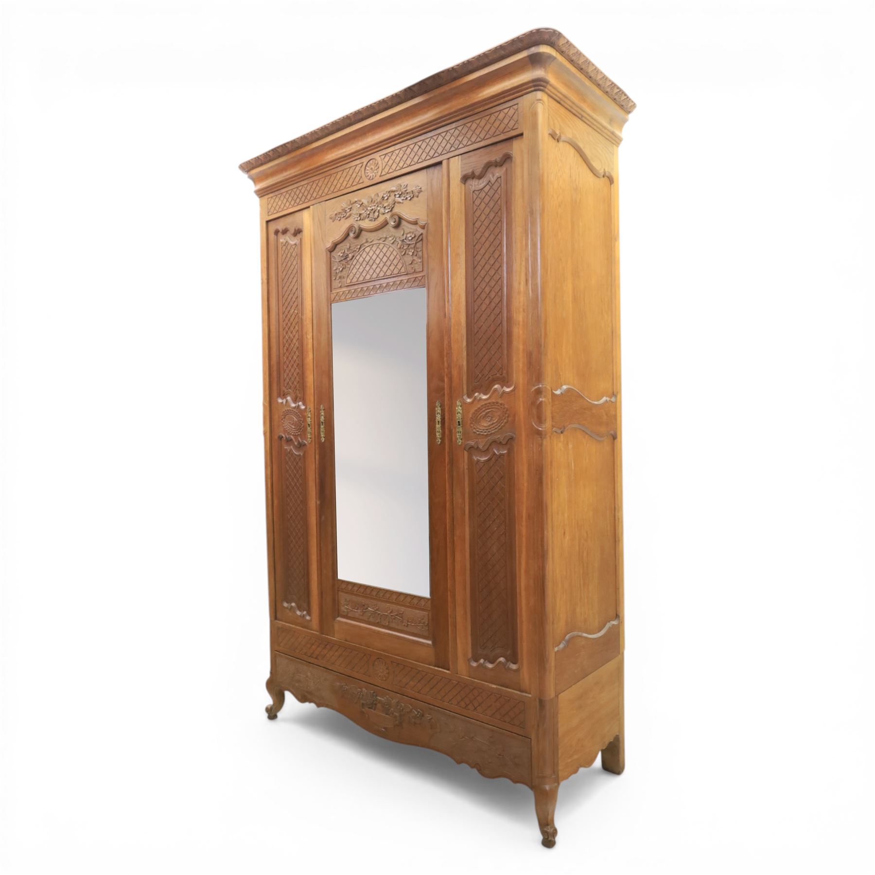 Early 20th century French oak triple door armoire, the moulded top above a frieze with carved lozenge decoration and central rosette, the central mirrored door enclosed by carved surround with floral crest, flanked by panelled doors with lattice carving, the base with shaped apron centred by carved basket motif, upon shaped cabriole supports