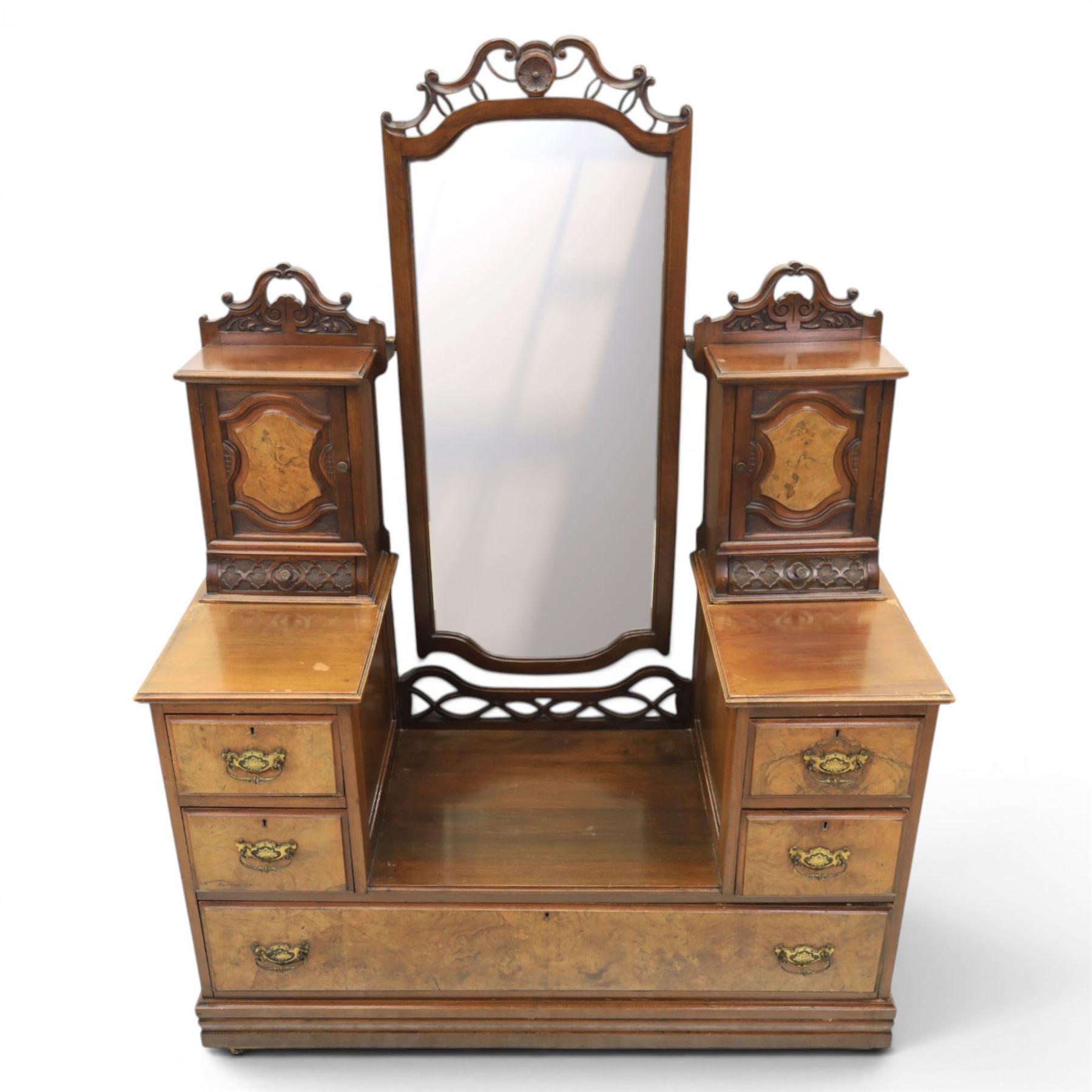 Edwardian figured walnut dressing chest, with central tilting mirror with pierced fret work, flanked by cabinet with figured walnut panelled door above a trinket drawer, with four short over a long long drawer, raised on a plinth base with castors 