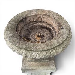 Pair of weathered cast stone Neoclassical design garden Kylix shape urns, foliate moulded rim over a gadrooned underbelly, the scalloped socle over a rectangular pedestal with faux-panelled sides, stamped with stylised ‘H’ monogram