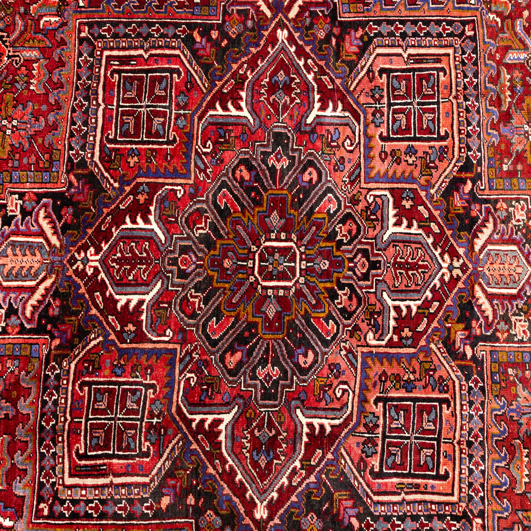 North West Persian Heriz hand-knotted carpet, brick red field, with large central angular star medallion with stepped outlines, surrounded by geometric floral devices and stylized rosettes, with corresponding corner spandrels, enclosed by a bold geometric main border with multiple guard stripes, with cotton fringe ends 