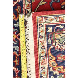 Persian Kashan crimson ground rug decorated with scrolling foliage, the indigo guard stripes with repeating stylised palmette motifs
