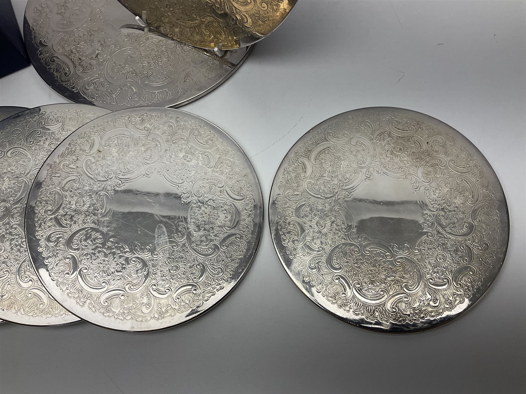 Set of eight silver plated placemats, each of circular form with engraved scroll and floral decoration, including two larger and six smaller examples, largest D23cm, in fitted case 