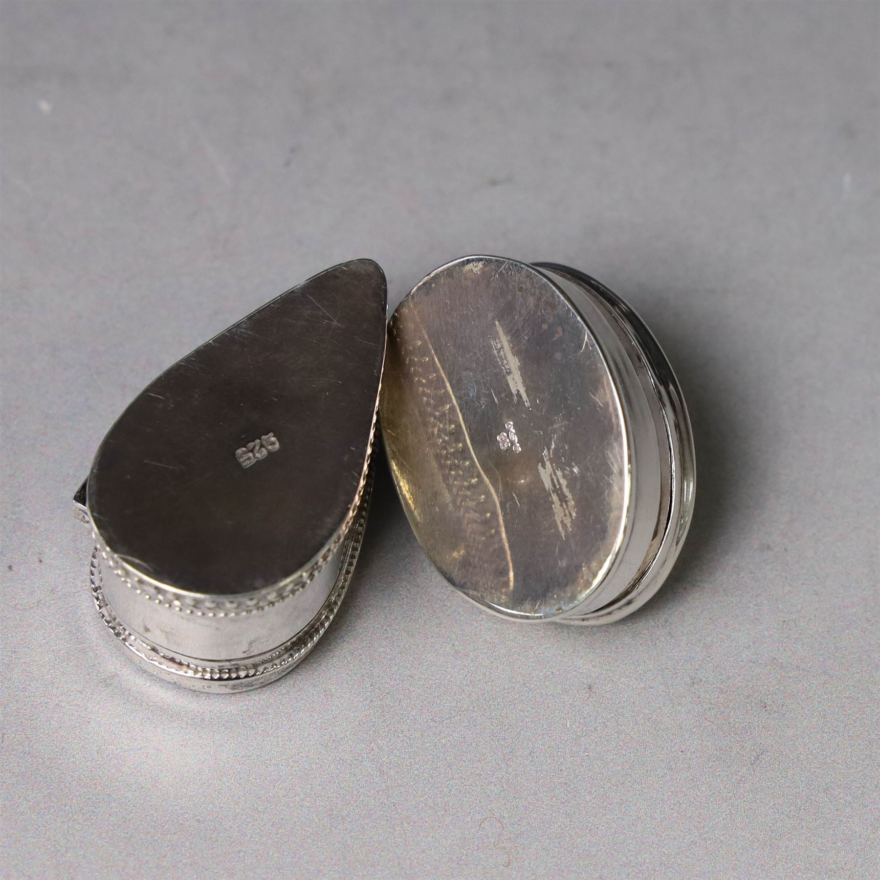 Two modern silver pill boxes, the first example of oval form, the hinged cover set with a tigers eye cabochon with beaded mount, and engraved scroll edge, hallmarked NC, London import 1995, W3cm, the second of teardrop form, the hinged cover set with lapis lazuli, marked 925, L3.5cm