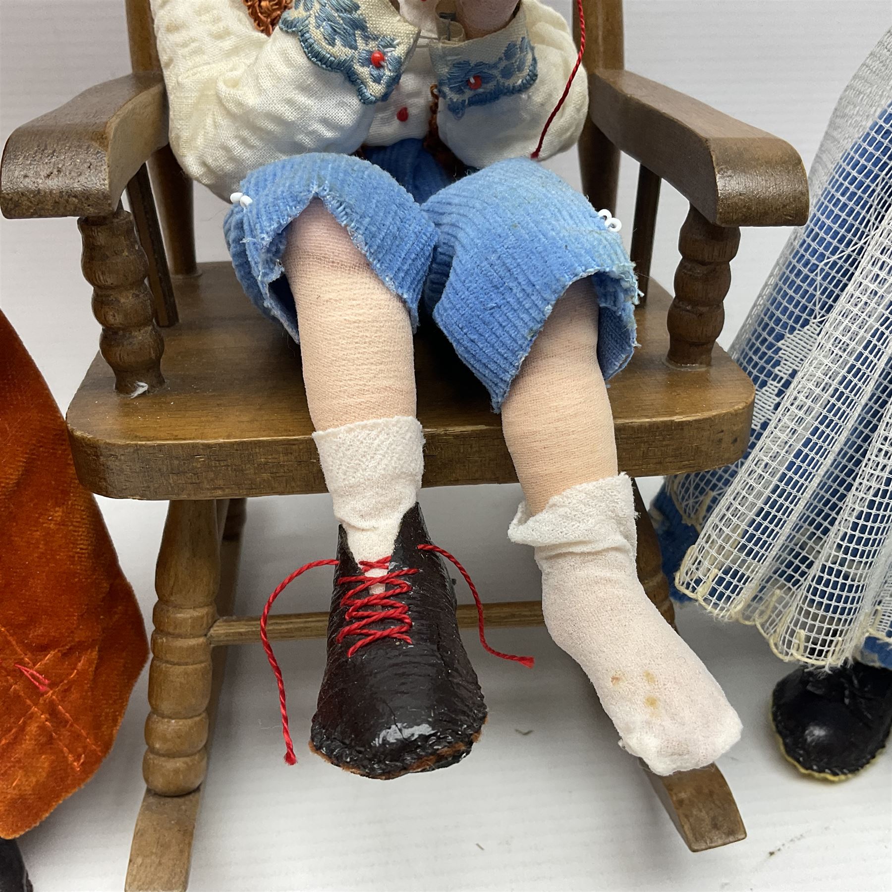 Anna Meszaros Hungary - three hand made needlework figurines - 'The Cobbler' as a child seated in a wooden rocking chair working on a removed boot H24cm; young girl standing crying holding a doll with broken head H32cm; and young girl in long dress and bonnet standing holding a doll H27cm (3)  Auctioneer's Note: Anna Meszaros came to England from her native Hungary in 1959 to marry an English businessman she met while demonstrating her art at the 1958 Brussels Exhibition. Shortly before she left for England she was awarded the title of Folk Artist Master by the Hungarian Government. Anna was a gifted painter of mainly portraits and sculptress before starting to make her figurines which are completely hand made and unique, each with a character and expression of its own. The hands, feet and face are sculptured by layering the material and pulling the features into place with needle and thread. She died in Hull in 1998.
