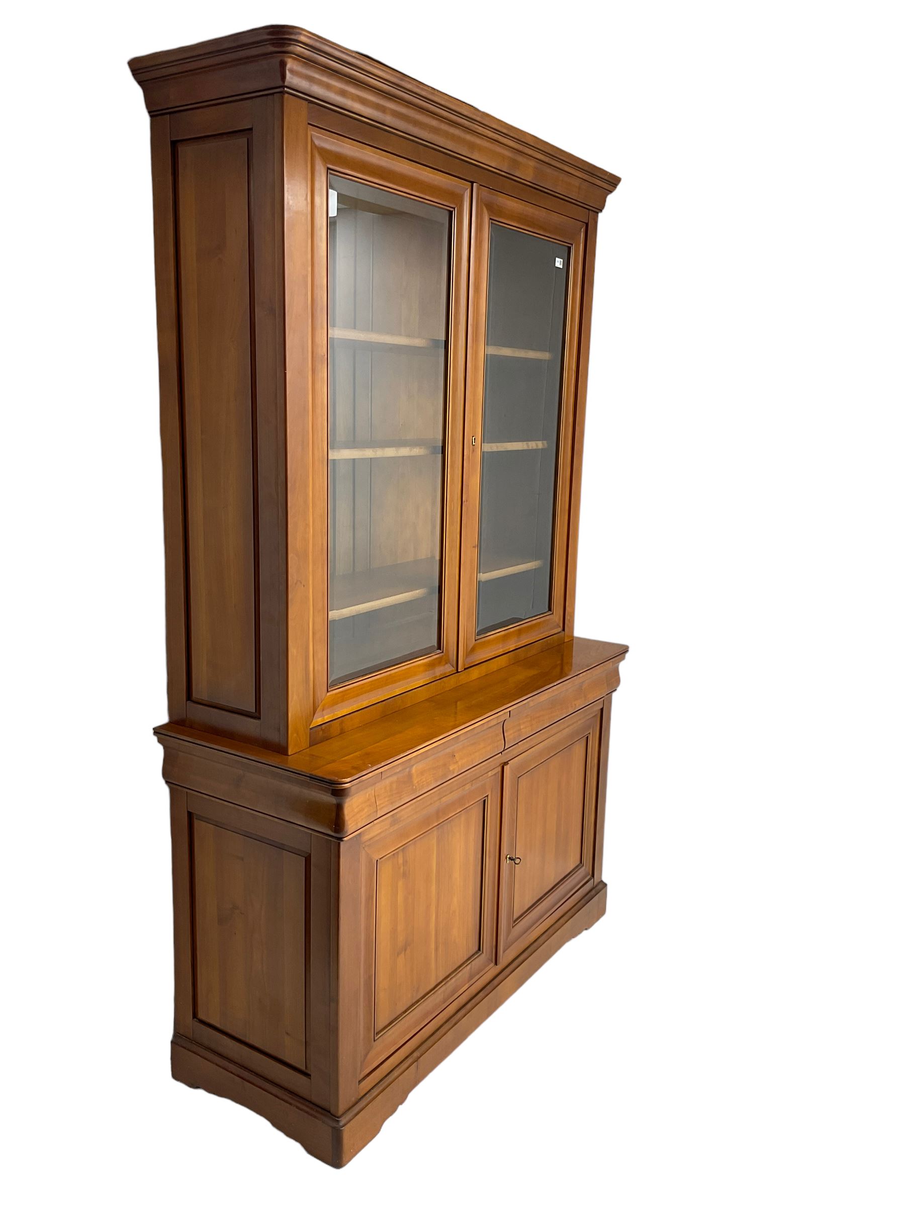 French cherry wood bookcase on cupboard, projecting cornice over two cupboard doors with bevelled glass panels enclosing three adjustable shelves, base fitted with two cushion drawers over double cupboard