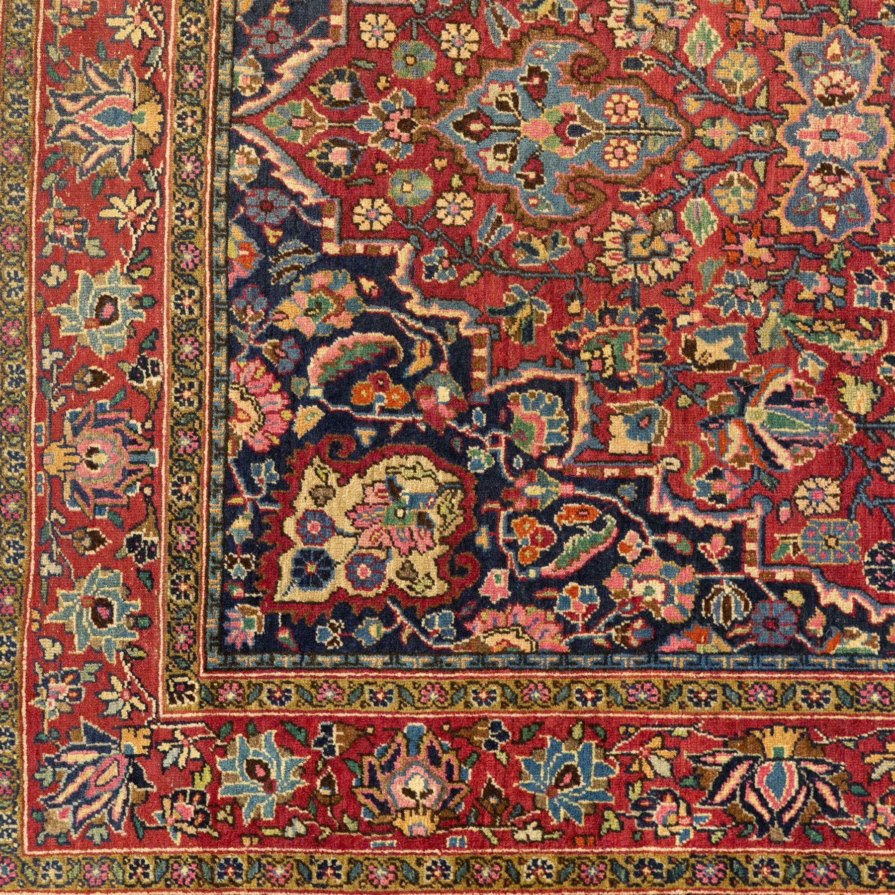 Persian Sarouk rug, richly decorated with an elaborate central medallion of palmettes and stylized floral motifs in indigo, ivory, and pastel tones on madder red ground, framed by spandrels, with a broad border of flowering palmettes and serrated leaves between a narrow floral guard border, fringe removed 