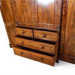 Early 19th century figured mahogany combination wardrobe, the breakfront architectural cornice over central press cupboard enclosing linen slides, flanked by full-height hanging cupboards with arched inset panels, lower arrangement of two short and two long drawers with turned knob handles, applied acanthus carved detail, raised on bun feet