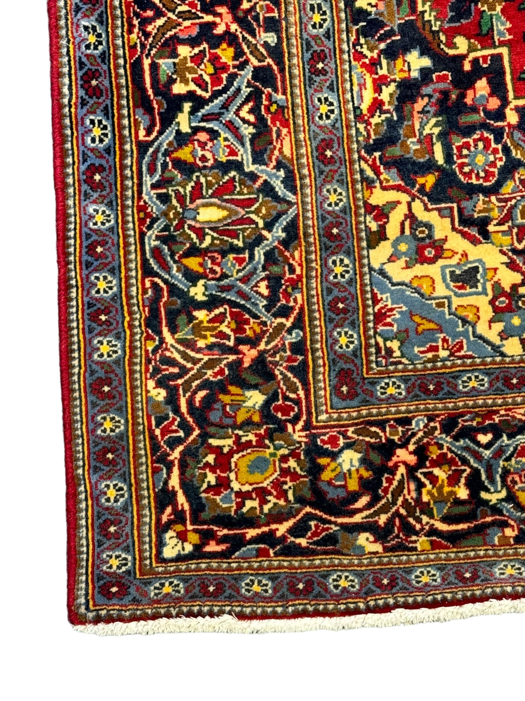 Central Persian Kashan crimson ground rug, central indigo pole medallion surrounded by sparsely placed bouquets interconnected with foliate branches, the guarded border with repeating palmette and Boteh motifs with interwoven scrolling patterns, framed by guard stripes