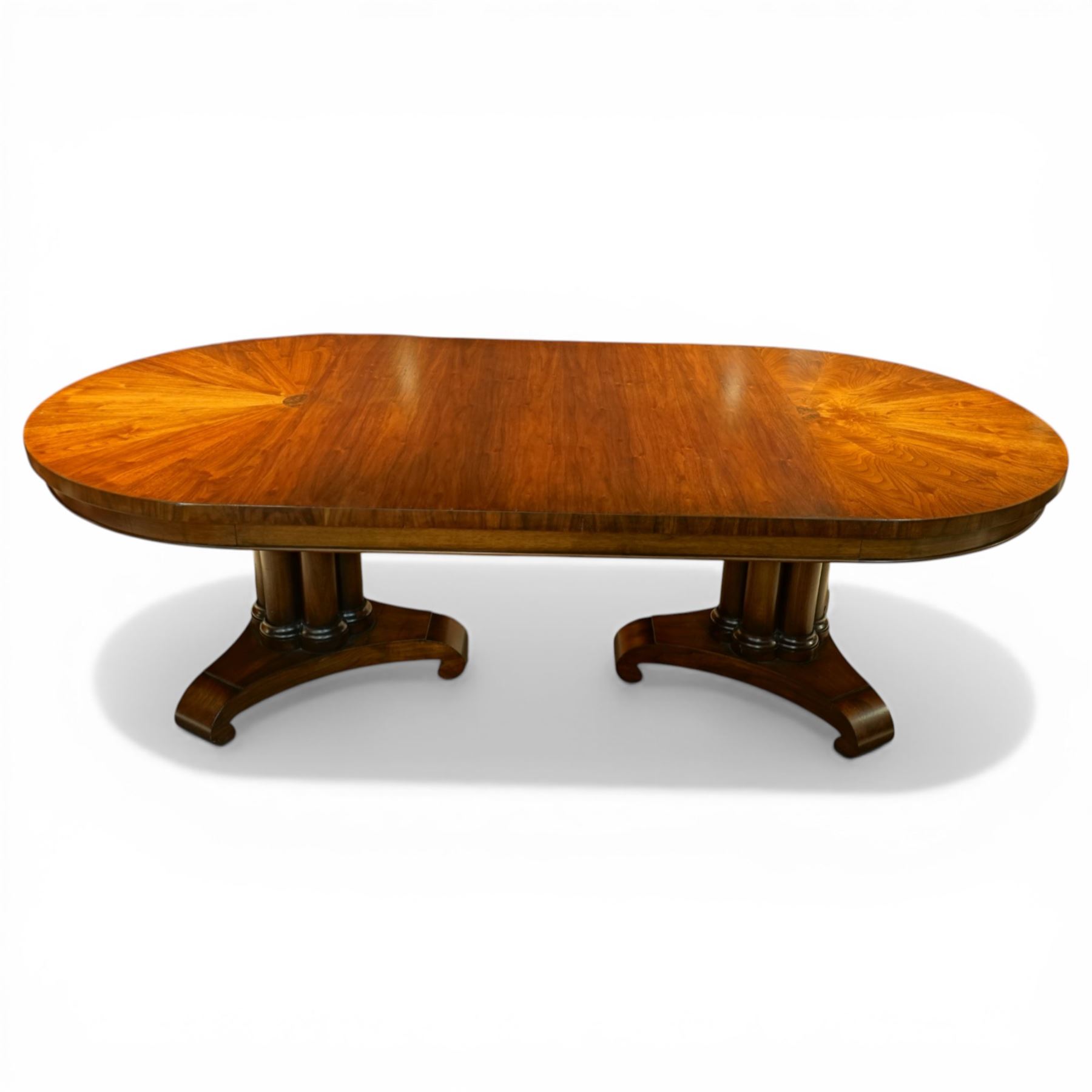 Late 20th century Regency design walnut twin pedestal dining table, the oval top with radial sunburst veneered ends centred by roundels, upon twin pedestal turned column supports, issuing to down swept triform bases