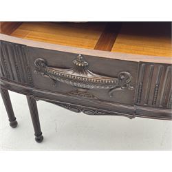 Early 20th century Hepplewhite style serving table, raised fleur-de-lis feather back with fluted detail and flower head mounts, the shaped top with carved foliate edge over single central drawer with applied urn motif, turned and reeded acanthus supports with recessed castors