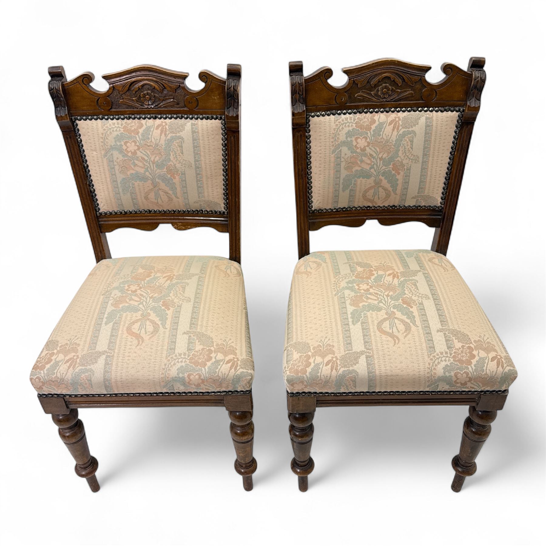 Victorian walnut set of four dining chairs, the shaped and carved top rails with central flowerhead and scroll decoration above upholstered backs and seats in floral woven fabric, brass stud trim, on ring turned front supports