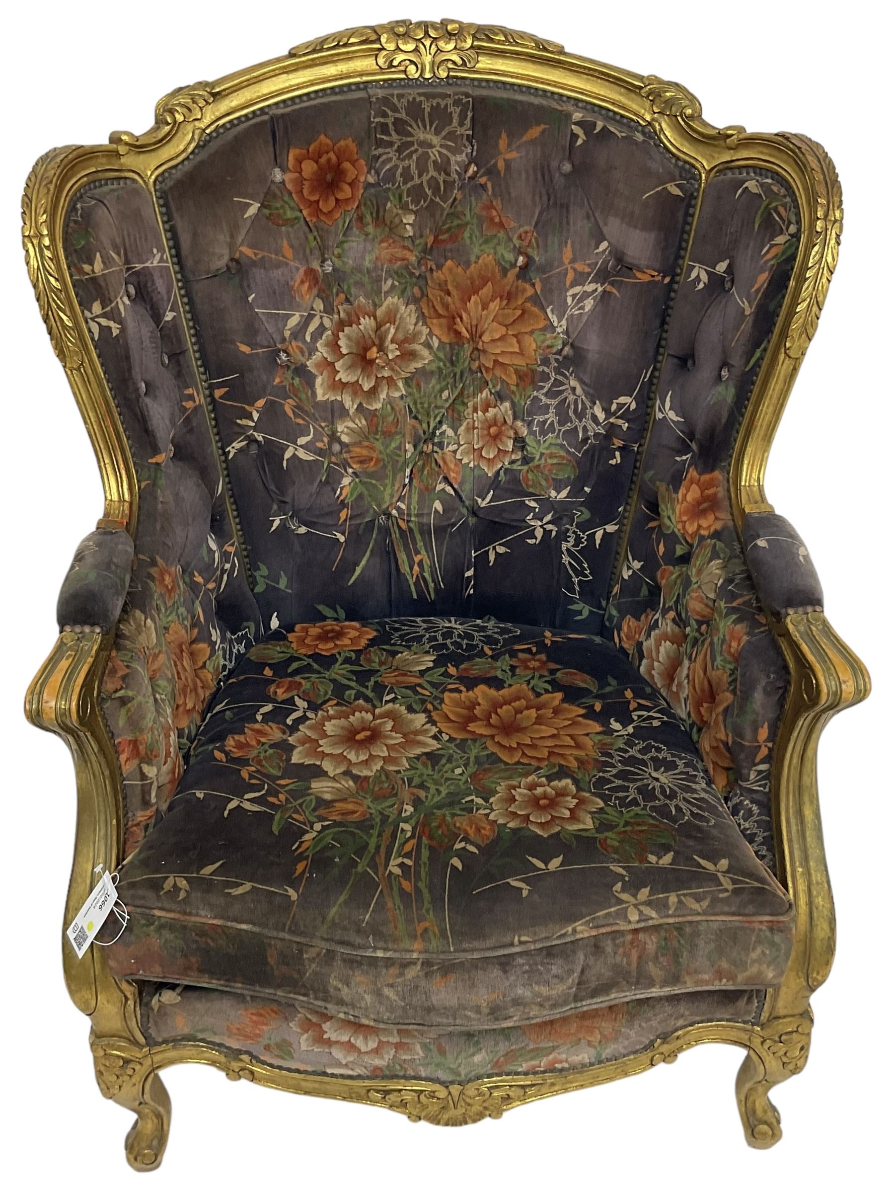 Pair of Louis XVI design gilt framed wingback armchairs, cresting rail carved and moulded with foliate decoration and C-scrolls, upholstered in buttoned floral patterned mauve velvet with loose seat cushion, scallop carved apron over cabriole supports