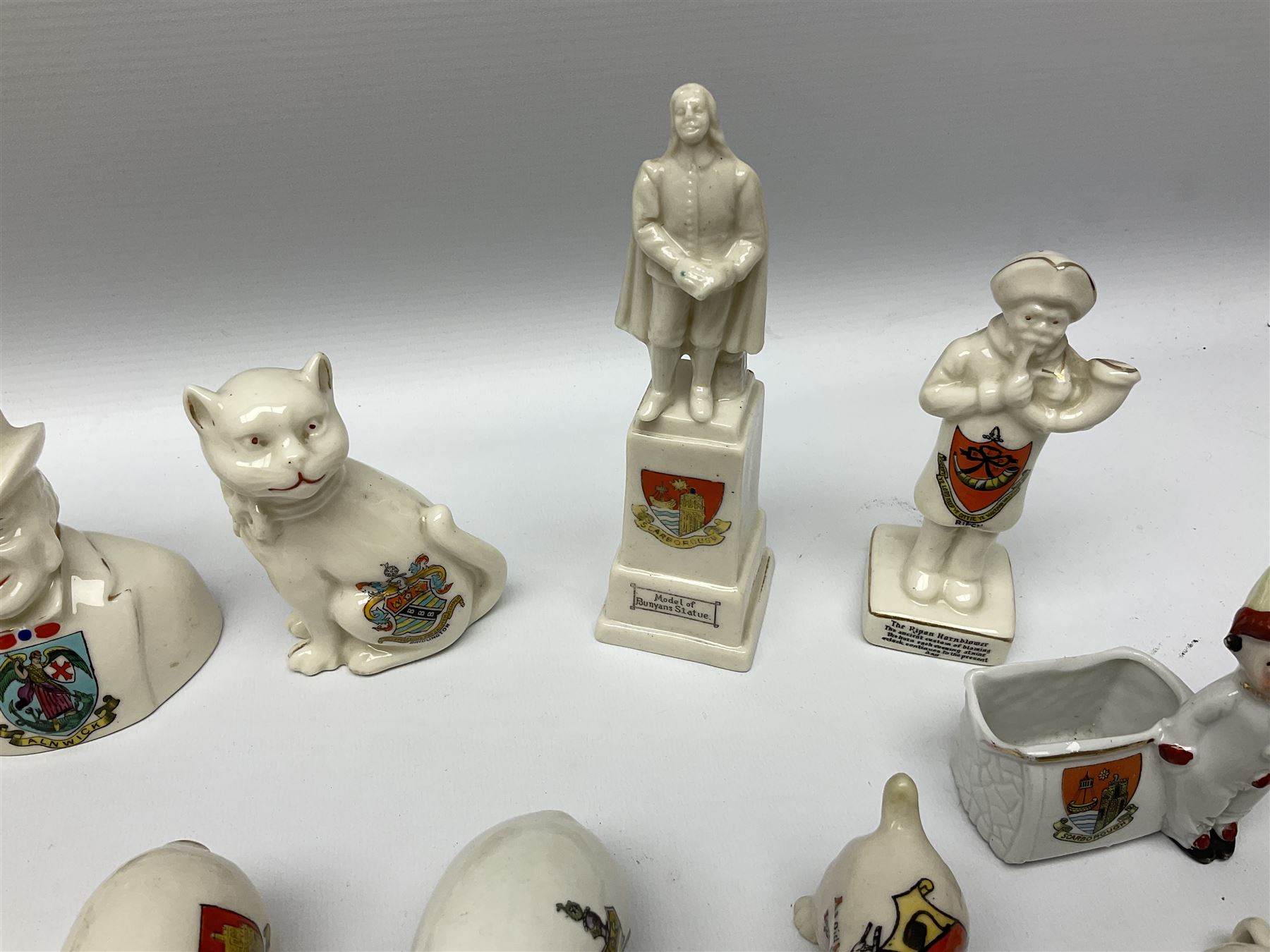 Collection of figural crested ware, to include Carlton Chins John Bull Alnwick, Clifton China Cheshire Cat,  Arcadia pig, Crafton crawling baby and another seated baby, quantity of cat, dog and pig figures, two Willow Art Model of Bunyans Statue, Toby jug, Victoria China, Arcadan bulldog, fish etc