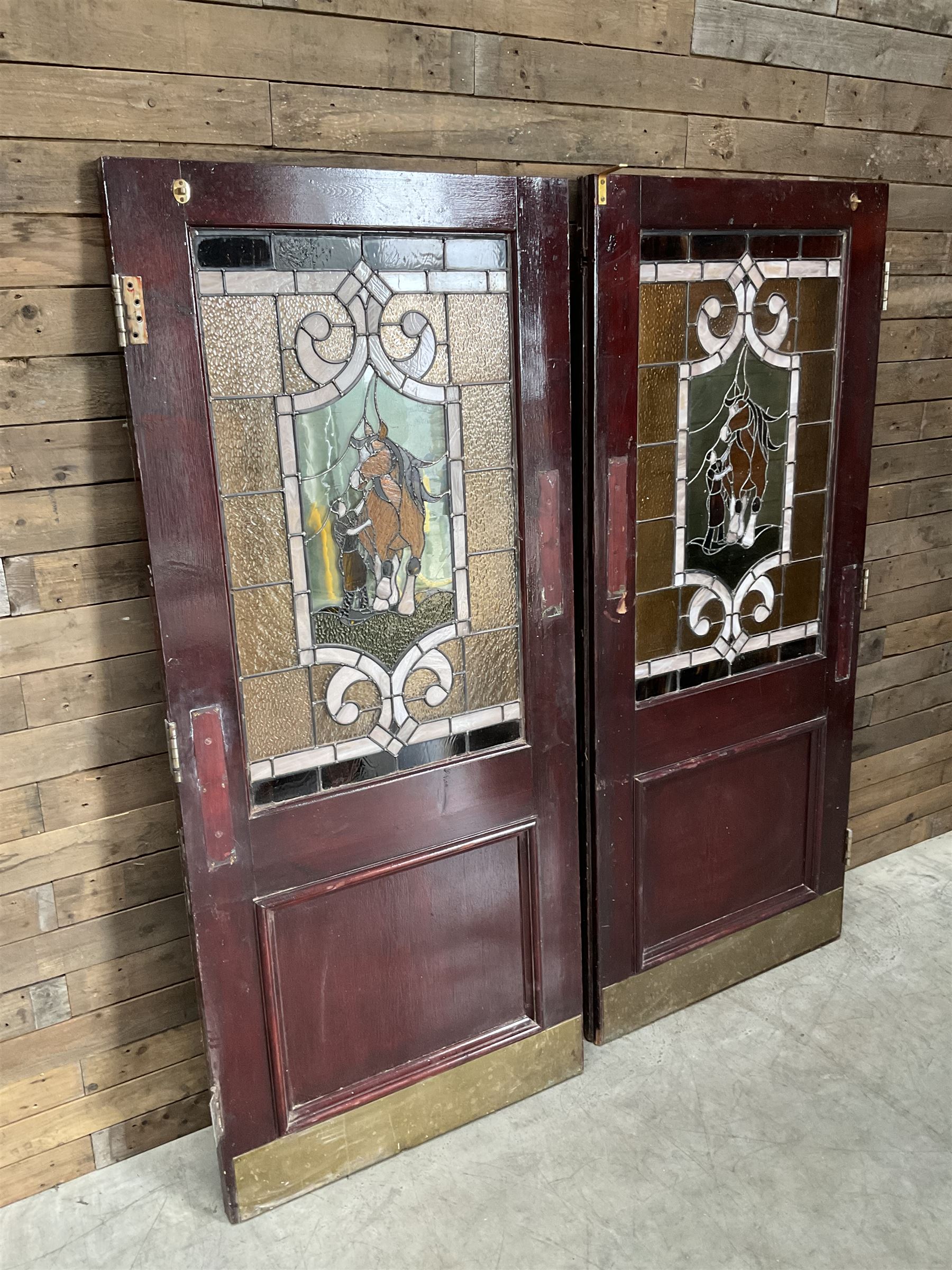 Two early to mid 20th century timber doors, set with lead framed stained glass panels depicting agricultural worker and horse