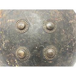 Indian black lacquered hide shield/dhal, of circular convex form fitted at its centre with four pierced iron bosses, each of hemispherical form with wide brims, the bosses corresponding on the inside with four iron rings for enarmes D53.5cm