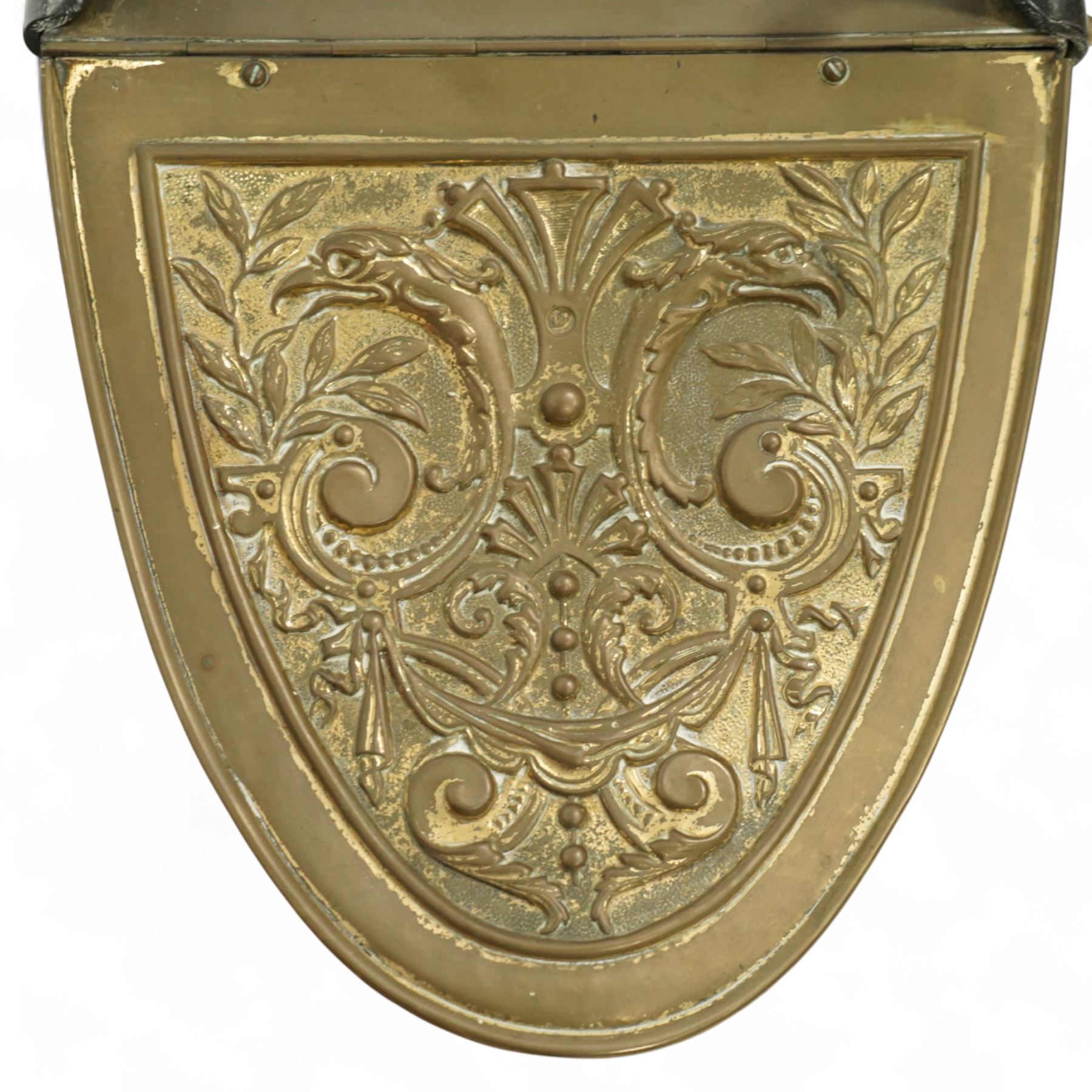 Late 19th century brass coal scuttle, of helmet form, with embossed scrolling foliate panels, cast iron supports with turned ebonised handle, raised on a cast iron tripod base
