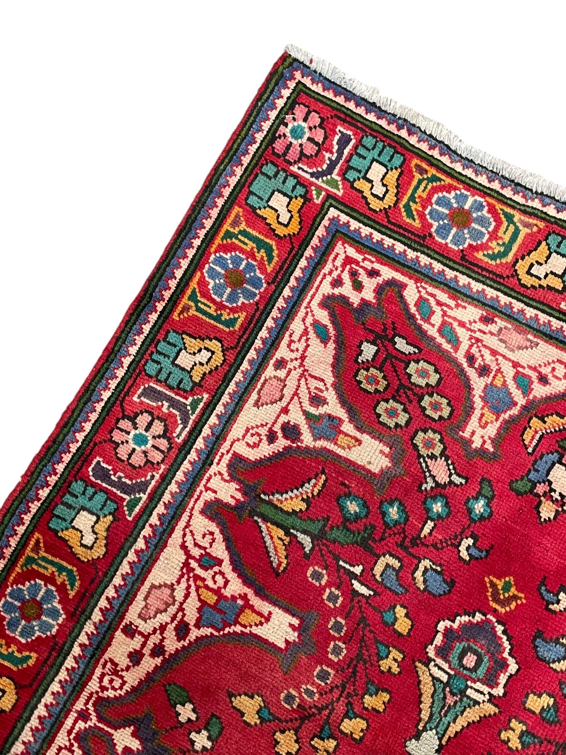 Persian Azerbaijan crimson ground rug, the field decorated with central floral motif and surrounded by trailing floral branches, enclosed within a shaped outer band with further floral decoration, the border with repeating flower heads, geometric guard stripes 
