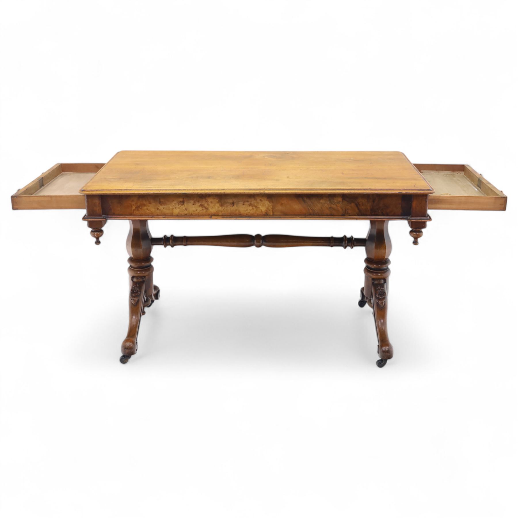 Mid Victorian walnut library table, plain top of rectangular form with moulded edge above frieze fitted with opposing drawers, table supported on a pair of turned and hexagonal carved baluster end standards, united by a turned stretcher terminating in scrolling sabre legs carved with acanthus and floral details, resting on ceramic castors, circa 1860