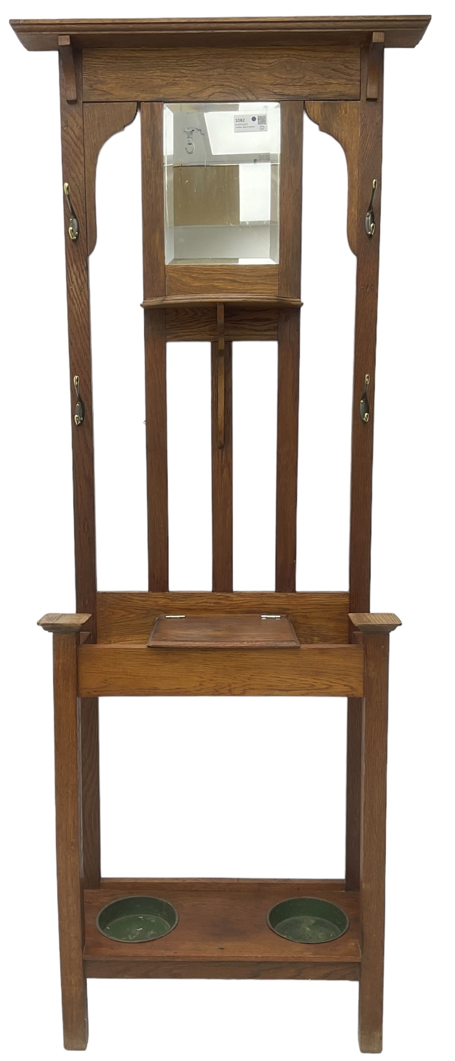 Edwardian oak hall stand, raised back with rectangular bevelled mirror plate surrounded by shelf and coat hooks, fitted with a glove box with hinged lid, over an undertier with two inset umbrella drip trays