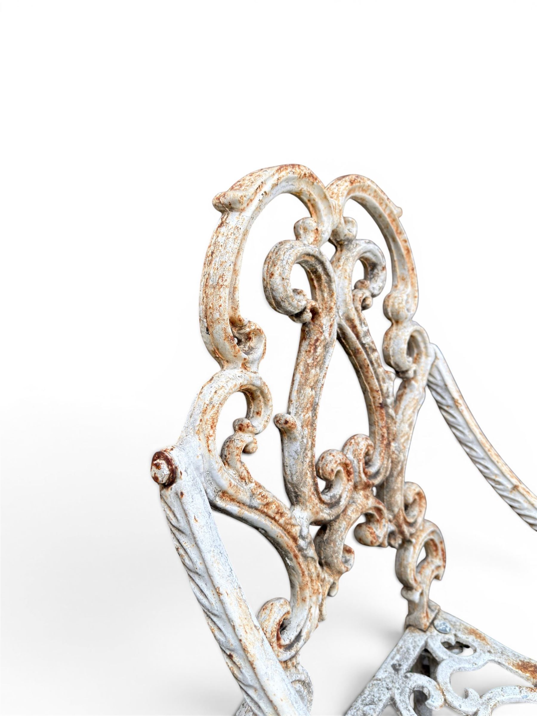 Pair of Victorian cast iron garden chairs, the ornate pierced back of scrolling foliate design, scrolling arm terminals over splayed supports formed of C and S-scrolls, in distressed white painted finish