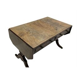 Regency mahogany sofa table, canted rectangular drop leaf top with walnut crossbanding, fitted with two frieze drawers with central lozenge decoration, two opposing false drawers, vasiform end supports with reeded edge and central roundel joined by ring turned and reeded stretcher, splayed supports on scaled brass cups and castors
