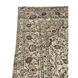 Persian Kashan ivory ground carpet, central medallion decorated with sixteen arranged palmette motifs, within a field decorated with swirling leafy branches and stylised plant motifs, the main border decorated with matching swirling pattern, within floral pattern guard stripes 
