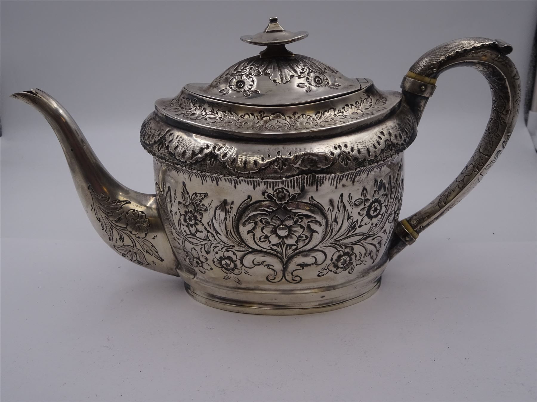 George III silver teapot, of oval form, with embossed foliate, floral and scroll decoration and engraved central cartouche, with acanthus capped C handle with ivory insulators, hallmarked John Emes, London 1807 This item has been registered for sale under Section 10 of the APHA Ivory Act
