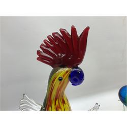 Three Murano style glass cockatoo parrots, the first with mottled yellow, red and orange body, clear outstretched wings, dark blue beak and red crest, raised upon clear stylised base, the second smaller parrot with merging blue and green body, and further with pink striped body, tallest H40cm