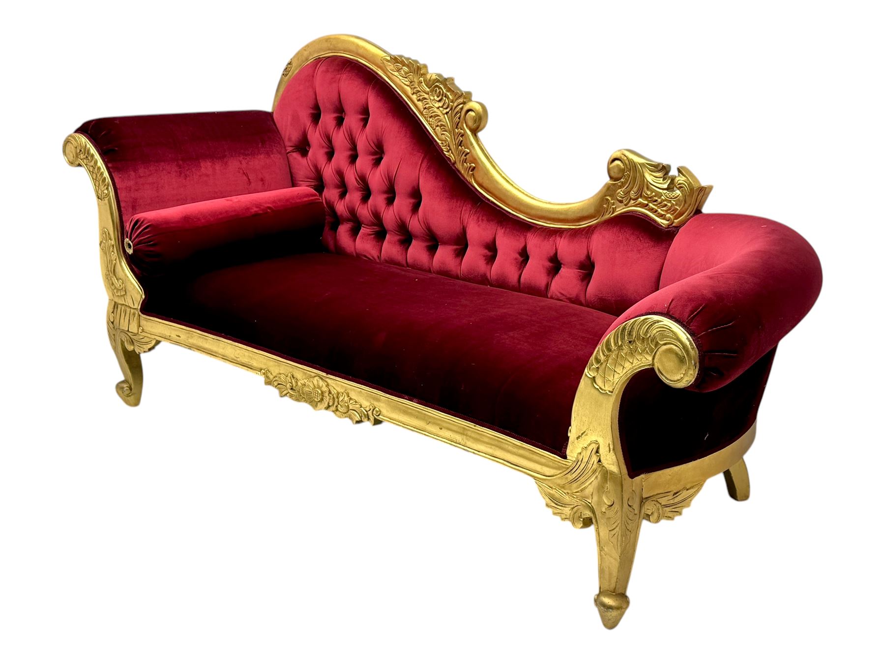Victorian design giltwood chaise longue, the curved backrest and seat upholstered in deep red velvet with tufted detailing, the frame carved with floral motifs and scrolling acanthus leaves, raised on shaped cabriole supports