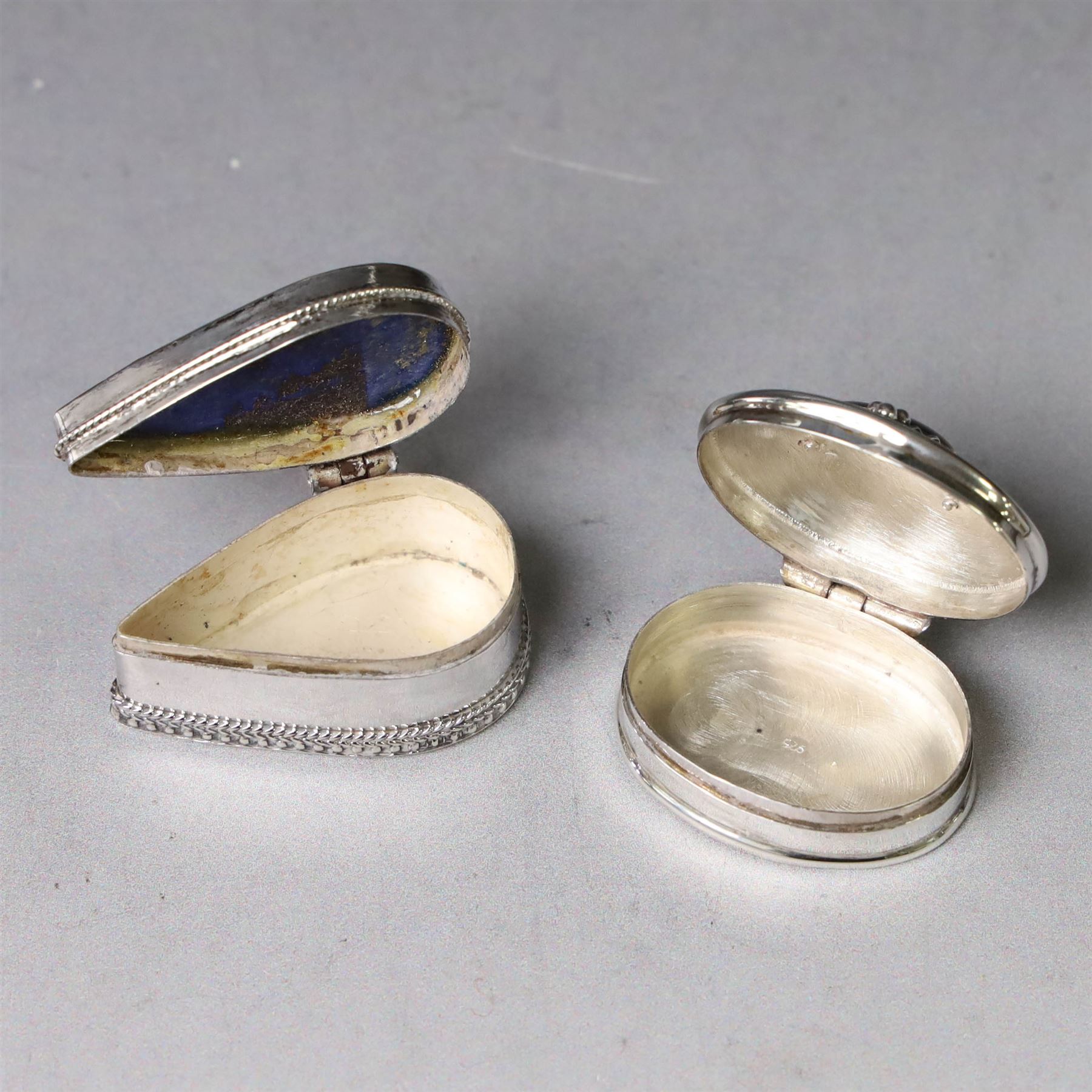 Two modern silver pill boxes, the first example of oval form, the hinged cover set with a tigers eye cabochon with beaded mount, and engraved scroll edge, hallmarked NC, London import 1995, W3cm, the second of teardrop form, the hinged cover set with lapis lazuli, marked 925, L3.5cm