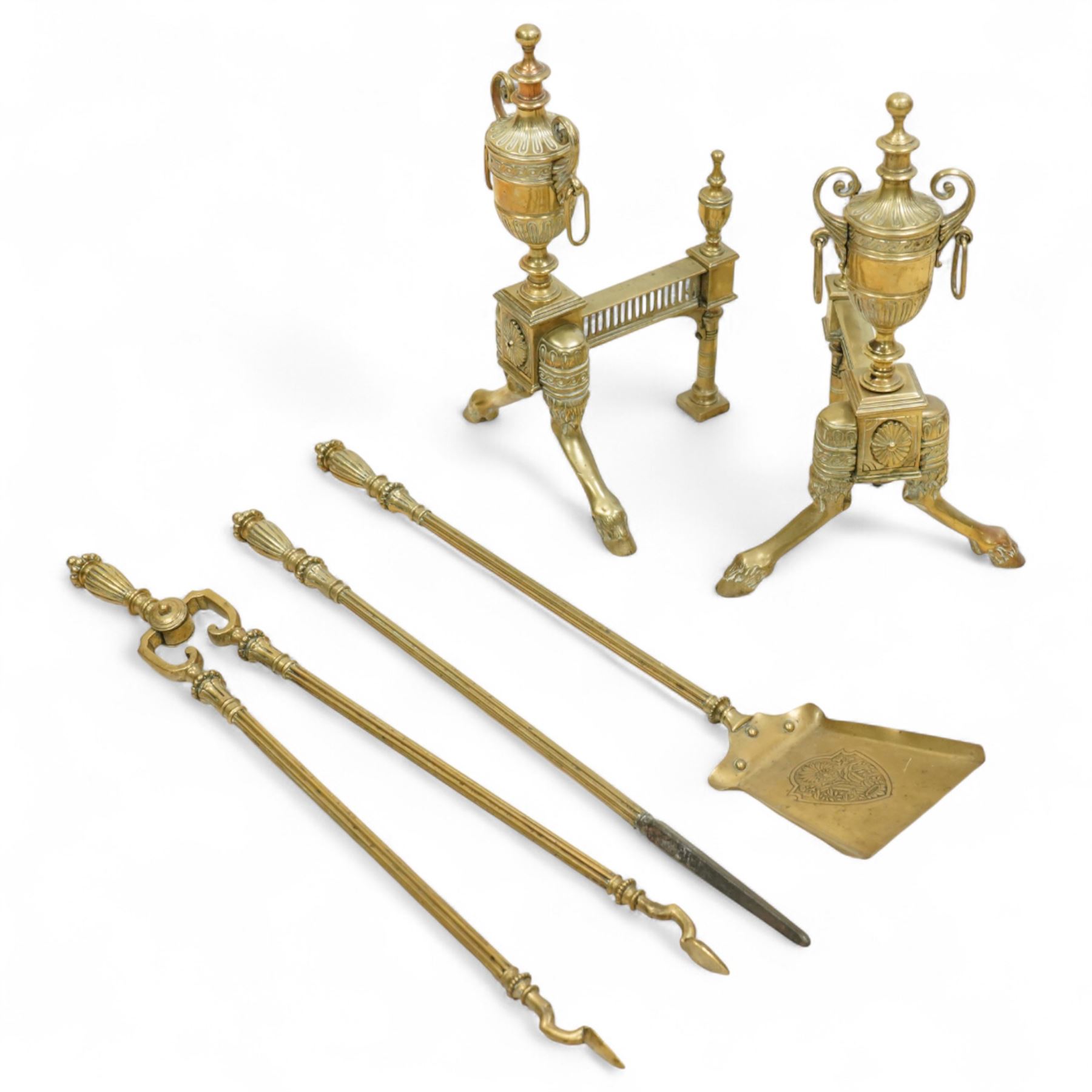19th century brass and iron fire dogs with fire irons, the fire dogs each with urn finials and arched legs, accompanied by three brass fire tools including shovel, poker and tongs with matching turned handles
