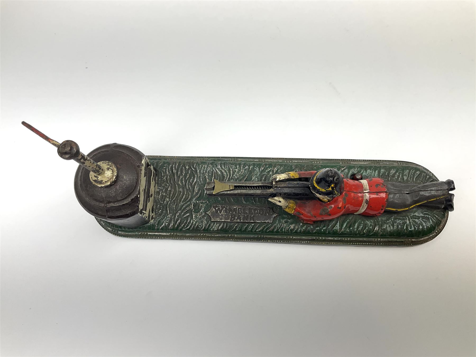 Very rare 19th century John Harper & Co. mechanical cast-iron money box, registered number 33821 patented 1885, inscribed on metal plaque 'Wimbledon Bank', based on the Queen's Trophy for shooting at Wimbledon, depicting a British Infantry man in red tunic and blue trousers lying on the ground using a gun to fire a brass coin launcher into a pill box with removable moving flag above L30cm