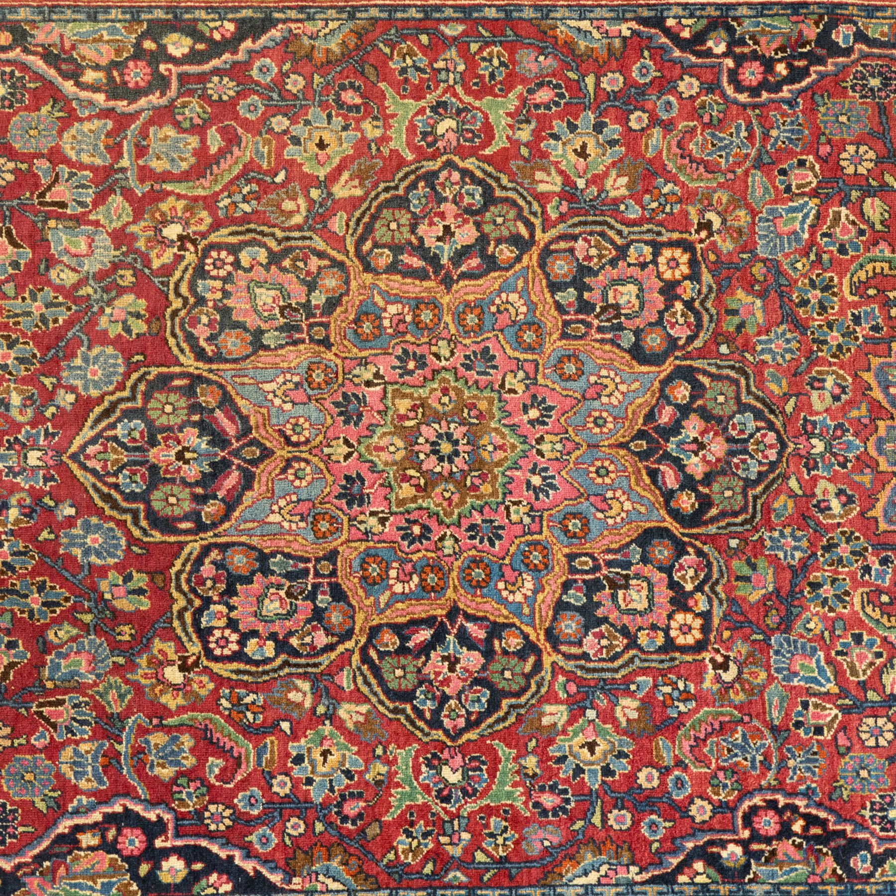 Persian Sarouk rug, richly decorated with an elaborate central medallion of palmettes and stylized floral motifs in indigo, ivory, and pastel tones on madder red ground, framed by spandrels, with a broad border of flowering palmettes and serrated leaves between a narrow floral guard border, fringe removed 