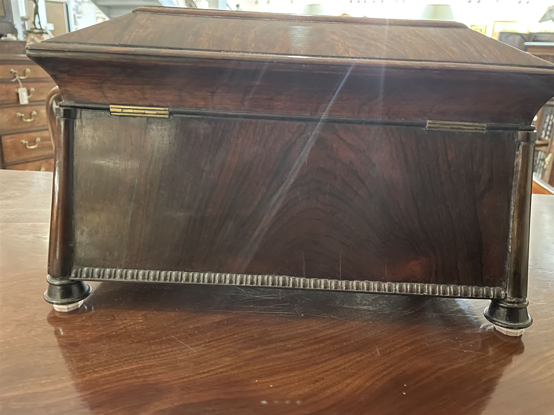 Early 19th century rosewood and brass inlaid tea caddy, of sarcophagus form, the front and hinged opening cover inlaid with brass scrolling panels, opening to reveal a compartmented interior with twin removable boxes with conforming inlaid brass detail to the hinged covers and zinc lining to the interiors, flanking a later glass mixing bowl, the whole upon four turned cylindrical feet, H21cm W36cm D20cm