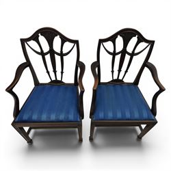 Set of eight George III style mahogany dining chairs, comprising two carvers and six singles, each with shaped top rail above pierced splay carved with feathers, with drop in stuffover seats upholstered in blue striped fabric, raised upon square tapering legs joined by stretchers, together with a mahogany twin pedestal dining table, the oval top with central leaf raised upon turned columns and splayed reeded legs terminating in lion paw feet and brass castors, 