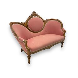 Late Victorian walnut framed double spoon back sofa, shaped crest rail with central carved medallion over curved back with pink upholstery, scrolling arms with additional carvings, on turned supports