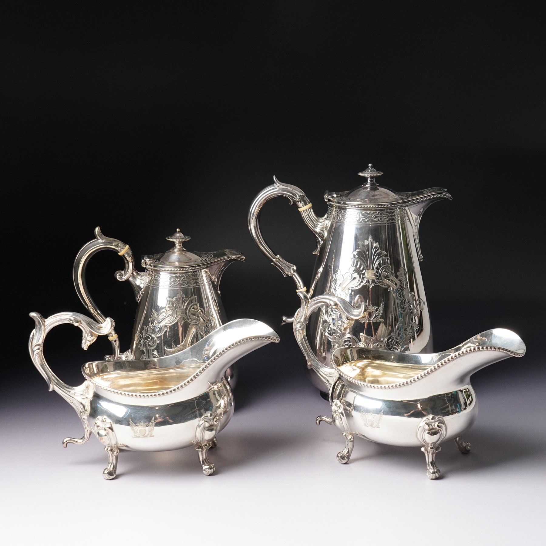 Pair of large silver plated sauce boats with bead edge decoration and C scroll handles engraved with a crest in the form of a winged heart and on shaped supports L20cm Maker probably Hawksworth Eyre & Co and an engraved hot water jug and a matching smaller jug with the same crest and by the same maker
