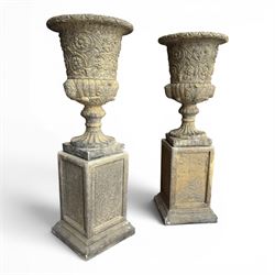 Pair of George III design antiqued composite stone garden urns of campana form, the egg-and-dart everted rim over a waisted body relief moulded with scrolling fruiting foliage and flowerheads, the gadrooned underbelly with twin mask ornaments, the knopped stems on fluted socles, raised on faux panelled square pedestal bases