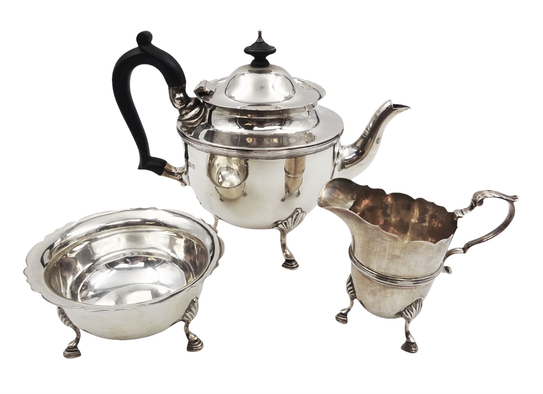 1920s three piece silver tea service, comprising teapot, with ebonised wooden handle and finial, milk jug and open sucrier, all of circular form, with shaped rims, and upon three hoof feet, hallmarked Wakely & Wheeler, London 1922, teapot H19cm