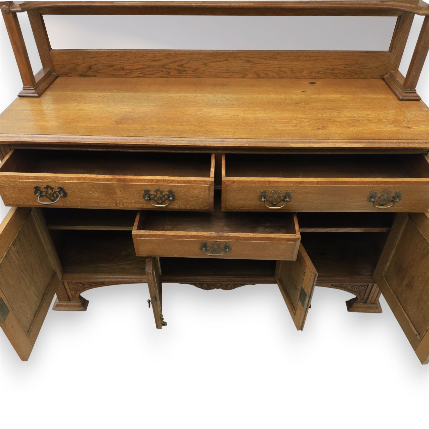 Arts and Crafts oak mirror back sideboard, the bevelled rectangular mirror set within a back with foliate carved panels, with turned baluster and knopped supports, upon a base with moulded top above three drawers  and three cupboard doors, two with carved foliate detail, upon four shaped bracket feet